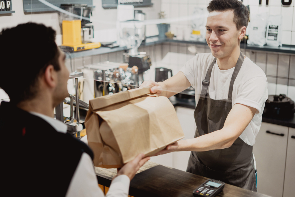 Buys lunch pizza and pasta in a paper bag with a takeaway. small business pizzeria coffee shop. a young male employee picks up dinner. convenient delivery in a corrugated cardboard box.