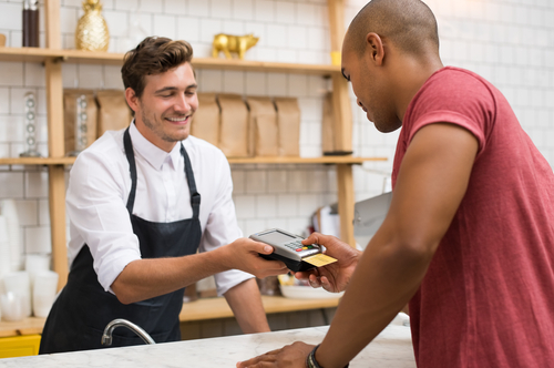 A server holds a credit card reader while a Black customer pays by credit card.