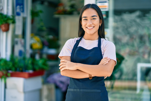 Young latin shopkeeper girl with arms crossed smiling happy standing at the florist