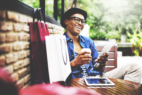 Happy customer sitting down after shopping while holding a coffee and smartphone.