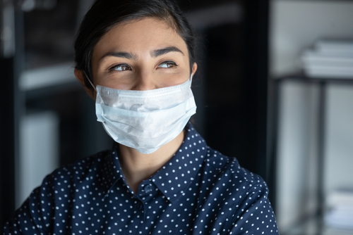 Hopeful smiling young woman in protective face mask look in distance hope for coronavirus pandemic end, happy millennial female in medical facial cover from COVID-19 thinking, healthcare concept
